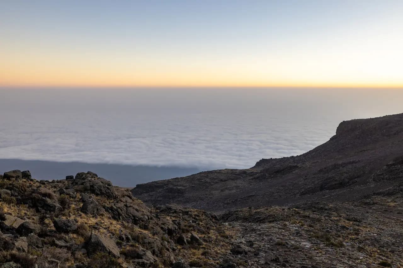 Panoramic view of mountain peak above clouds at sunrise with rocky terrain in foreground